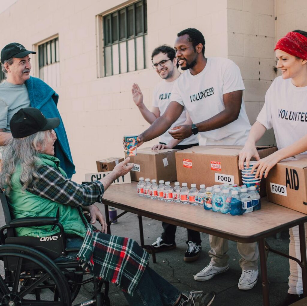 Volunteers distribute bottled water and supplies to diverse individuals in an outdoor setting, showcasing community support.